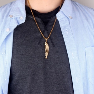 Détail d'un collier pendentif arête de poisson doré porté sur le cou d'un mannequin