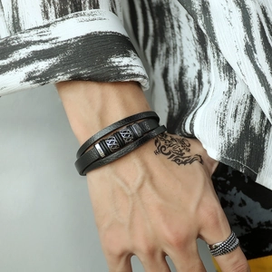 Detail of multi-layered black leather bracelet with silver metal charms on male wrist