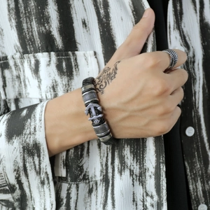 Detail of multi-layer braided leather bracelet with silver anchor and textured ring