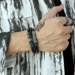 Close-up of layered leather bracelet with cross beads and silver ring on model's hand