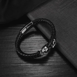 Detailed view of men's leather braided bracelet featuring silver skull charms and magnetic clasp