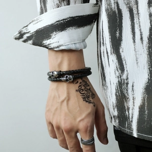 Close-up of men's multi-layer braided leather bracelet with silver skull charms and magnetic clasp