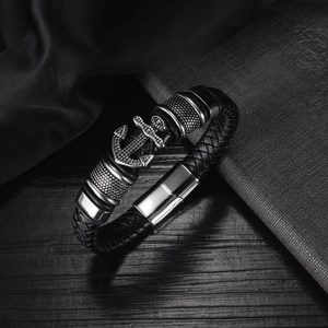 Macro detail of men's anchor leather bracelet with silver accents on dark wood surface