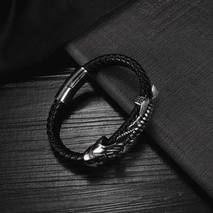 Macro detail of braided black leather bracelet featuring a silver metal dragon head charm