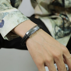Primo piano di un bracciale da uomo in pelle nera intrecciata con placca in acciaio lucido