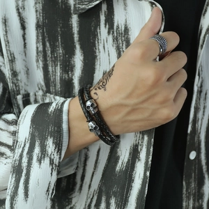 Close-up of double-layer braided black leather bracelet with silver skull charms and ring