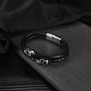 Detail of multi-layer braided black leather bracelet with vintage metal skull charms