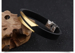 Detail of black silicone men's bracelet with golden brushed metal plate on wood