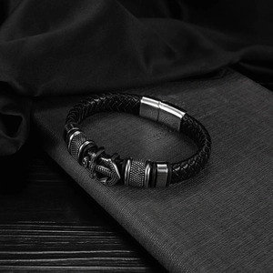 Vintage black braided leather bracelet with metallic anchor charm on textured background