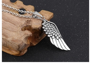 Close-up of vintage silver angel wing pendant with detailed texture on a wooden stand