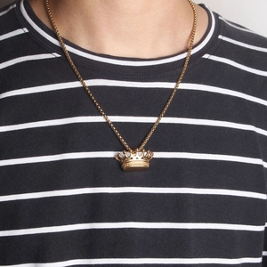Detailed close-up of a 3D gold crown pendant necklace worn on a striped shirt