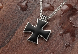 Macro view of silver stainless steel iron cross pendant with black enamel on wood