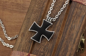 Close-up of gothic silver and black iron cross pendant resting on a vintage wooden chest