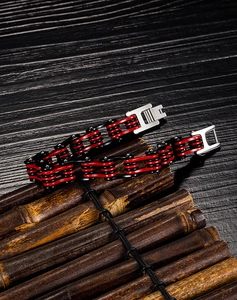 Détail du bracelet chaîne de moto en acier rouge et noir sur fond de bambou foncé