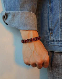 Détail d'un bracelet chaîne de moto noir et rouge porté avec une veste en jean