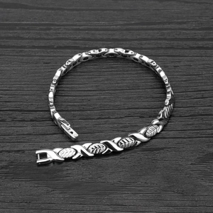 Polished silver magnetic leaf bracelet with X-shaped links on a dark wood background