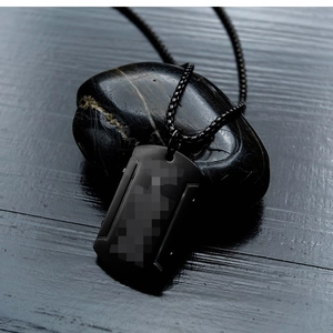 Vue détaillée d'un pendentif militaire en acier inoxydable noir mat sur une pierre texturée