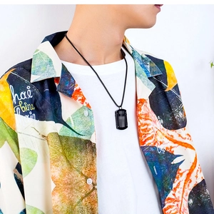 Gros plan d'un collier avec pendentif plaque noire sur un mannequin en chemise fleurie