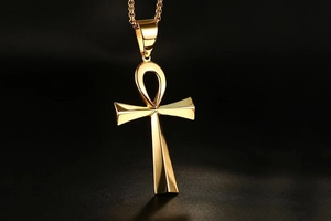 Macro shot of polished gold Ankh cross pendant with box chain on dark background