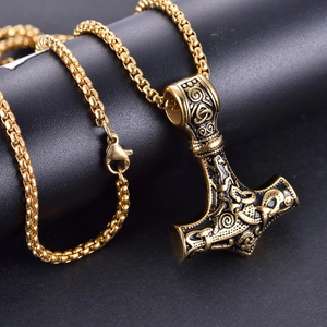 Macro side view of gold Viking Mjölnir pendant with intricate Nordic engravings on box chain