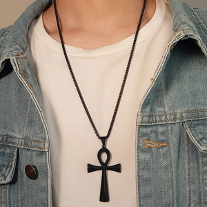 Close-up of black Ankh cross pendant on ball chain necklace worn over white T-shirt