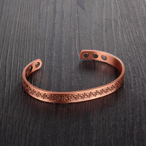Vintage magnetic copper therapy bracelet with Greek meander engraving on wood background