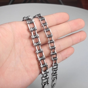 Bracelet motard en acier inoxydable et silicone noir tenu à la main sur fond gris épuré