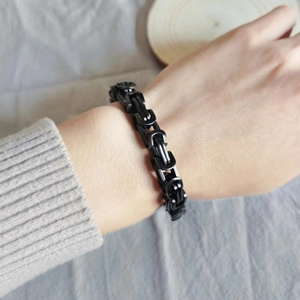 Close-up of matte black Byzantine chain bracelet worn on wrist with grey knit sleeve