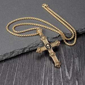 Close-up of gothic gold-finish cross necklace with skull detail on stone background