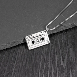 Detailed view of vintage cassette tape pendant with square box chain on texture background