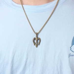 Detailed close-up of a vintage gold trident pendant necklace worn on a light blue shirt