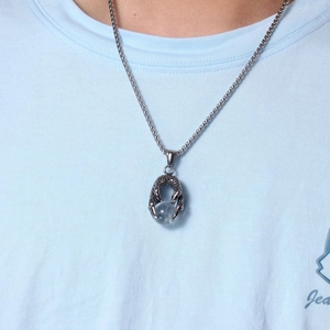 Gros plan d'un pendentif griffe de dragon tenant une perle bleue sur chaîne en acier