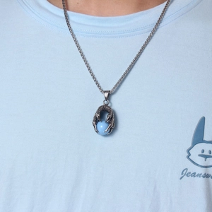Détail du pendentif griffe de dragon argenté tenant une perle bleu clair sur chaîne carrée