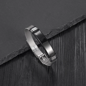 Detail of adjustable silver mesh bracelet with polished black metal plate on rock surface