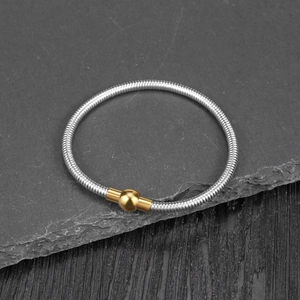 Close-up of a silver snake-textured spring bracelet with a gold magnetic ball clasp