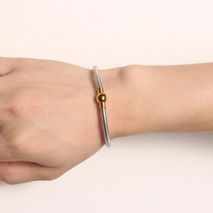 Detail view of a two-tone stainless steel snake chain bracelet with a gold bead accent