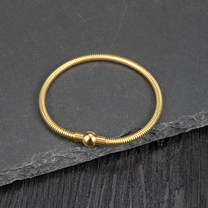 Detail of gold snake bone spring bracelet with polished bead on dark stone texture