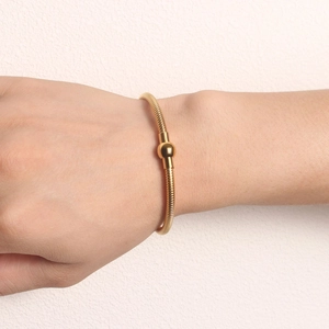 Close-up of golden spring snake chain bracelet with polished metal sphere on wrist