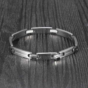 Detail of matte silver-grey brushed stainless steel link bracelet on dark wood surface
