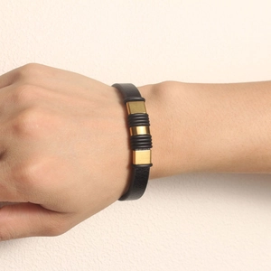 Detailed view of a black PU leather bracelet with gold metal accents on a wrist