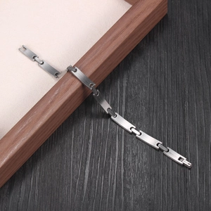 Minimalist stainless steel chain bracelet with matte finish displayed on a wooden frame