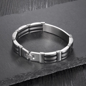 Detail of men's stainless steel bracelet with black silicone lines on a dark stone surface