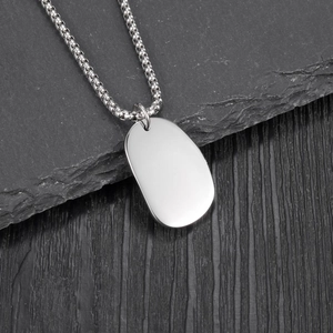 Collier pour homme avec pendentif ovale en acier poli et chaîne à billes sur fond rocheux