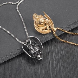 Vue détaillée des pendentifs crâne ailé en finitions or et argent sur fond d'ardoise