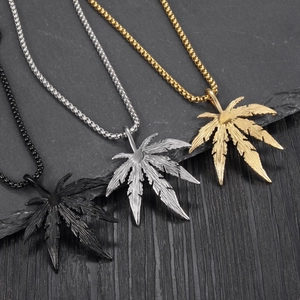 Détail des pendentifs feuille en noir, argent et or sur fond d'ardoise texturée