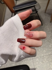 Macro shot of dark red glossy nails with colorful glitter and red heart patterns