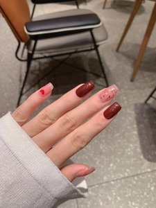 Detailed view of long square wine red nails with heart patterns and glitter accents