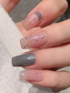 Close-up of minimalist pink and grey press-on nails with spotted patterns and gold glitter