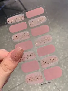 Macro detail of glitter gradient nail stickers in pink and gold applied to the thumb
