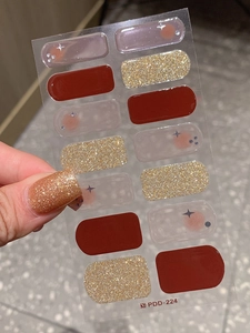 Close-up of gold glitter nail sticker on thumb with red and starry translucent designs